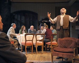 The Berger family (seated l-r, Victor Talmadge, Rebecca White, Charles Dean, Anthony Nemirovsky, Patrick Russell, Ellen Ratner) has dinner while Jacob (r, Ray Reinhardt) talks to Moe (l, Rod Gnapp) in Awake and Sing! Photo by David Allen