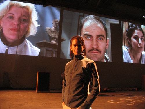During a rehearsal, director Kim Collier stands on the No Exit set, with the cast (from left: Lucia Frangione, Andy Thompson, and Laara Sadiq) projected on screens behind her. Photo by Nathan Medd.
