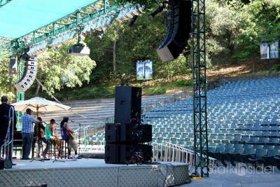 The outdoor theater is surrounded by lush landscaping, soaring trees.