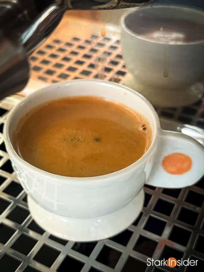 Espresso dripping into a warm mug under the group head, with crema just beginning to bloom.