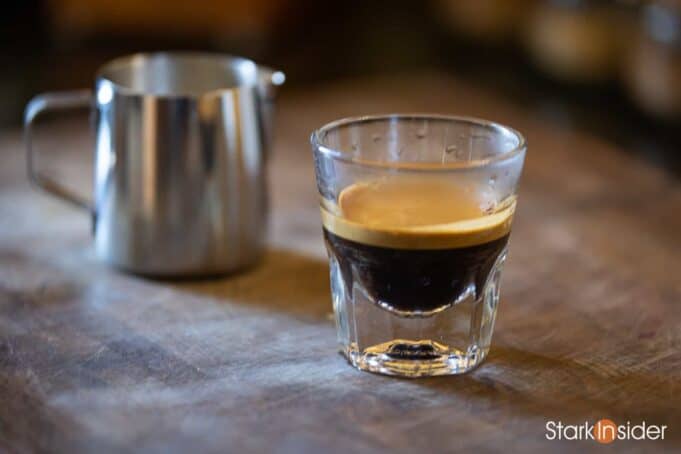 Close-up of espresso shot in glass cup with milk pitcher in background