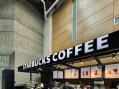 Trendspotting: Starbucks Drops Fall 2025 Menu – PSL Returns Aug. 26 with New Pecan Cortado Leading the Charge Starbucks coffee kiosk with illuminated signage and a “Line Starts Here” sign, representing launch of the Fall 2025 menu