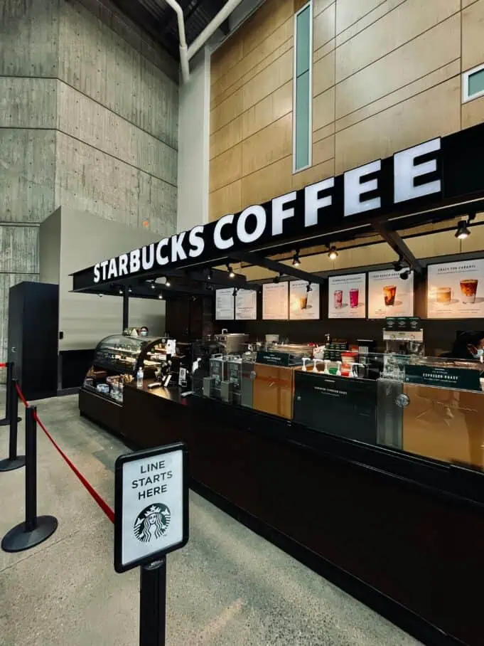 Starbucks coffee kiosk with illuminated signage and a “Line Starts Here” sign, representing launch of the Fall 2025 menu