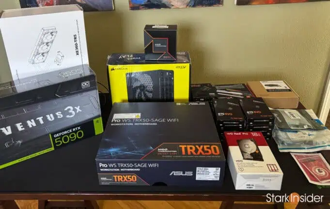 AI lab hardware parts laid out on table including RTX 5090 GPU, ASUS TRX50 motherboard, and Threadripper box.