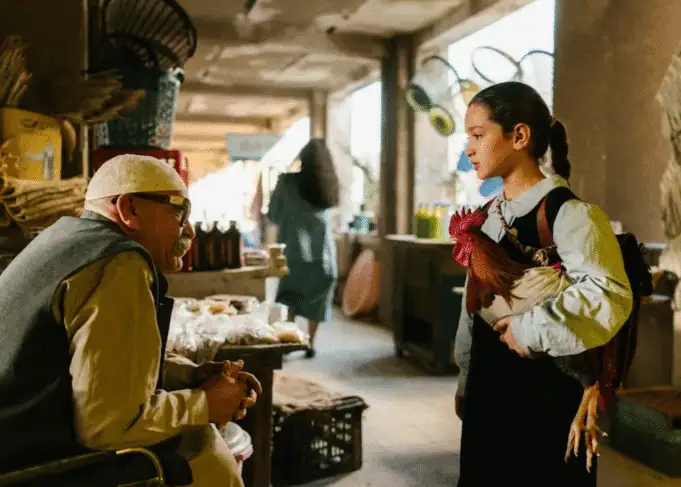 Scene from The President’s Cake — Lamia (Baneen Ahmad Neyyef) speaks with a vendor while holding a rooster in an Iraqi market.