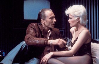 Why Brian De Palma’s ‘Body Double’ Deserves a Second Look Scene from Brian De Palma’s Body Double (1984) with a woman in black lingerie talking to a man in a leather jacket on a bed in a Hollywood apartment high above Los Angeles, California.